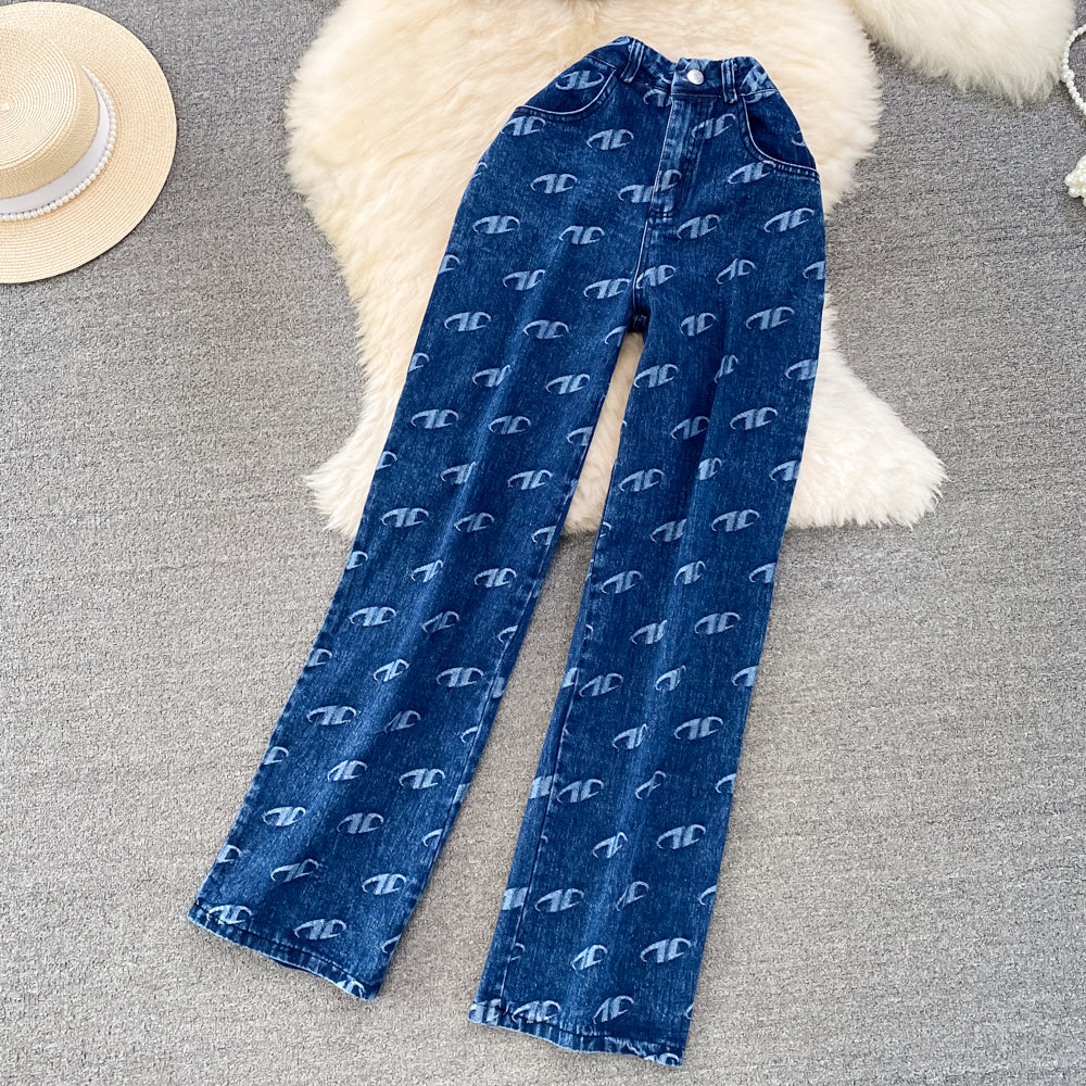 Blue denim jeans with a pattern on a gray surface with a white rug and straw hat.