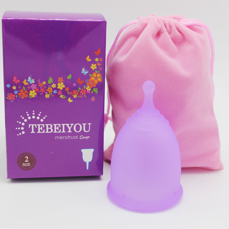 Purple menstrual cup with packaging and pink drawstring bag on a white background