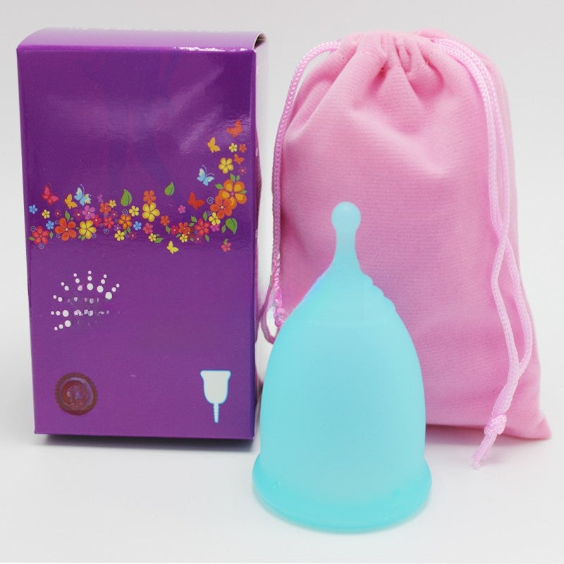 Turquoise menstrual cup with purple packaging and pink drawstring bag on a white background